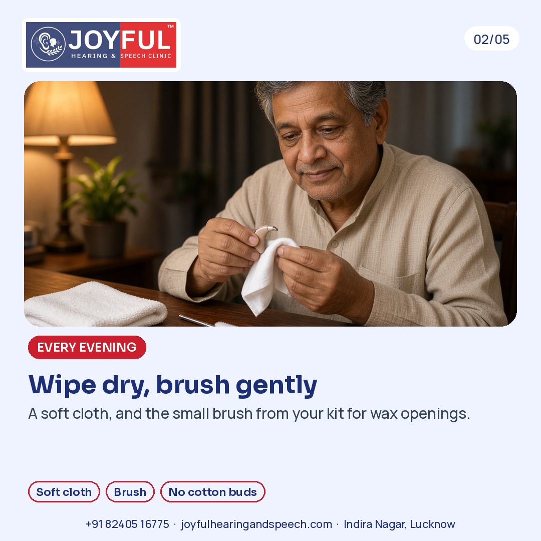 A man wipes a hearing aid with a soft cloth; a small brush and towel lie on the table.